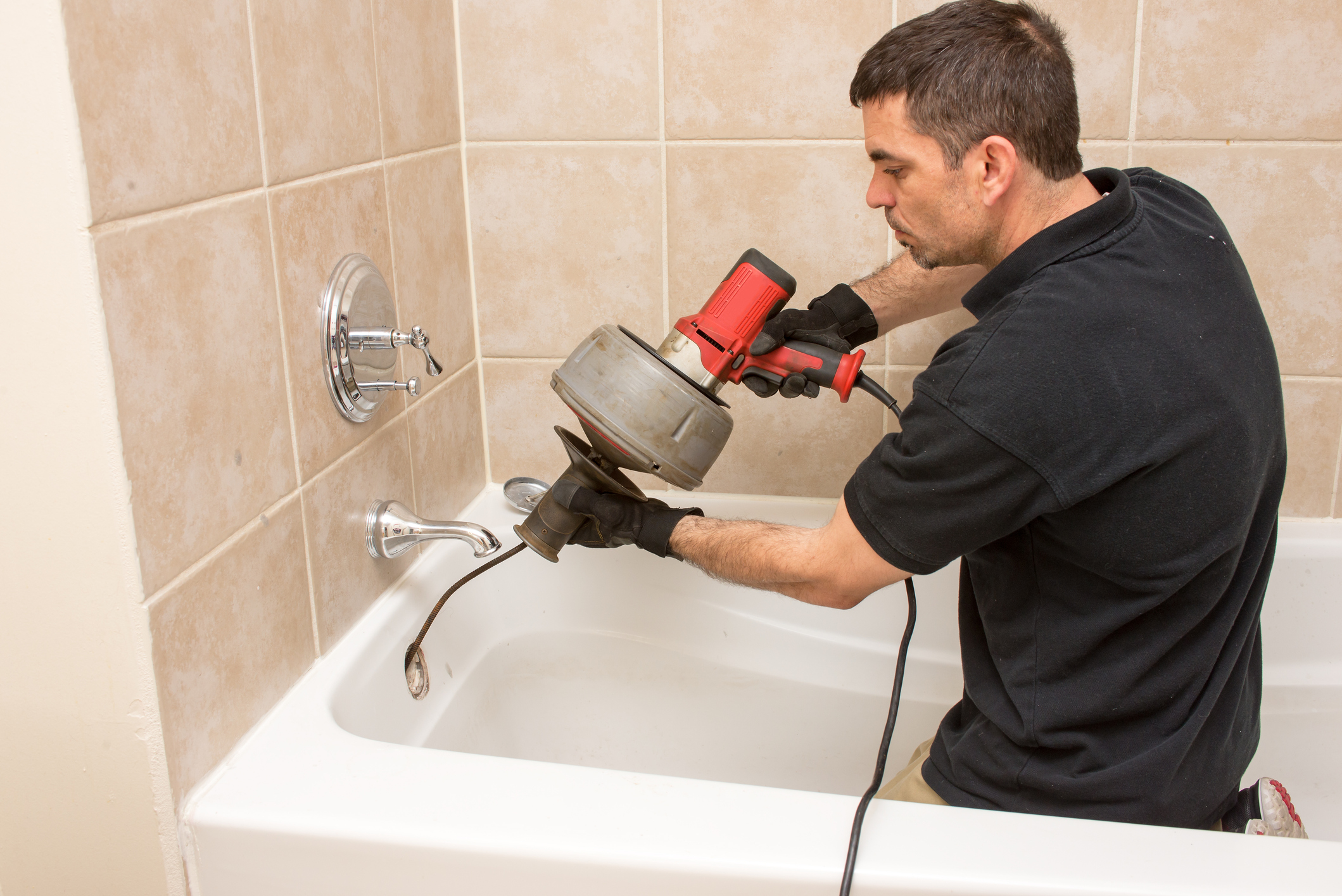 A professional plumber in Michigan performing drain cabling in a clogged bathtub drain.