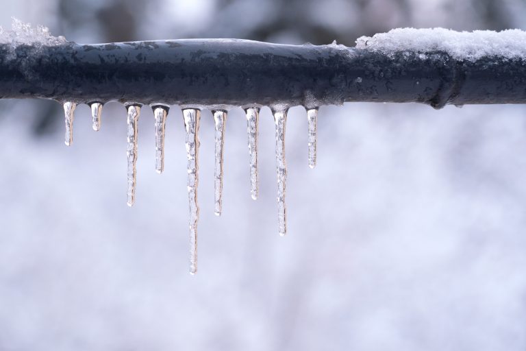 Photo of a pipe, frozen solid with icicles hanging from it.