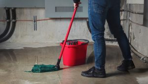 Cleaning up after a basement flood: mature Michigan homeowner with a mop cleans water after a sump pump failure