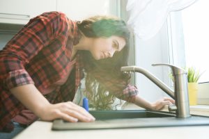 A woman leaning over her kitchen sink to investigate a rotten egg smell coming from the drain.