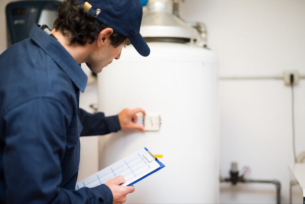 A plumber checking a water heater to diagnose a rotten egg smell in a home's hot water.