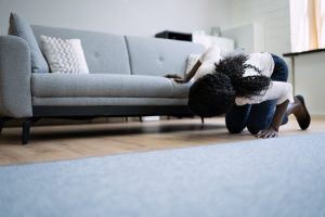 Homeowner kneeling to check a warm, discolored spot on their living room floor caused by a hidden slab leak