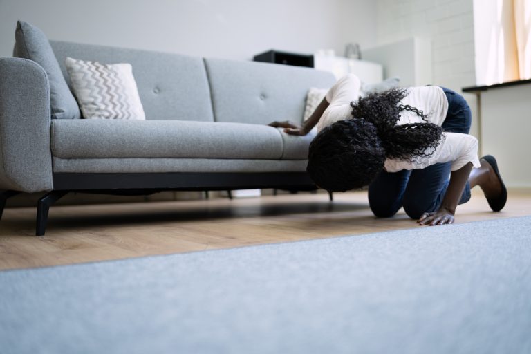 Homeowner kneeling to check a warm, discolored spot on their living room floor caused by a hidden slab leak